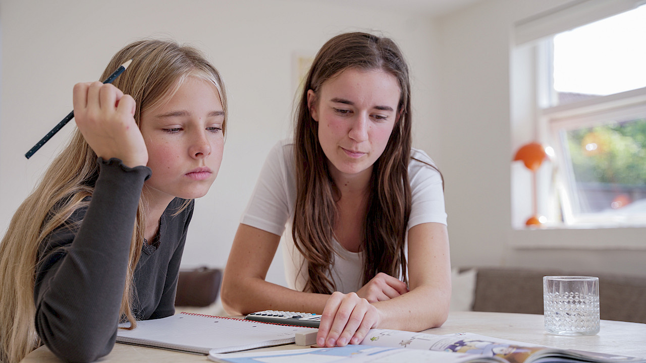 Elev får hjælp til lektier af mentor ved bord derhjemme