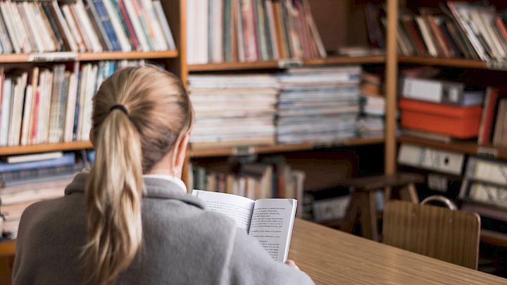 Elev sidder og læser på bibliotek