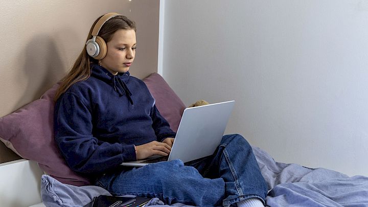 Pige sidder i seng og læser lektier på computer