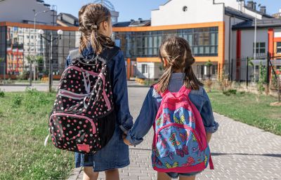 Et billede af to piger, med rygsække på, som holder i hånden 